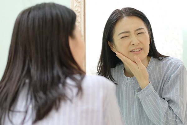 歯の痛みで頬を押さえている女性の写真