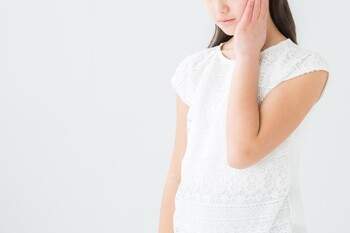 痛みを感じて頬を押さえている女性の写真