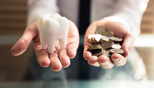 歯の模型とコインをそれぞれの手に持っている写真