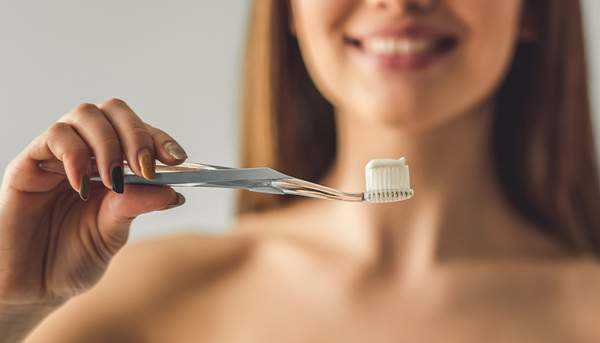 女性が歯磨き粉をのせた歯ブラシを持っている写真